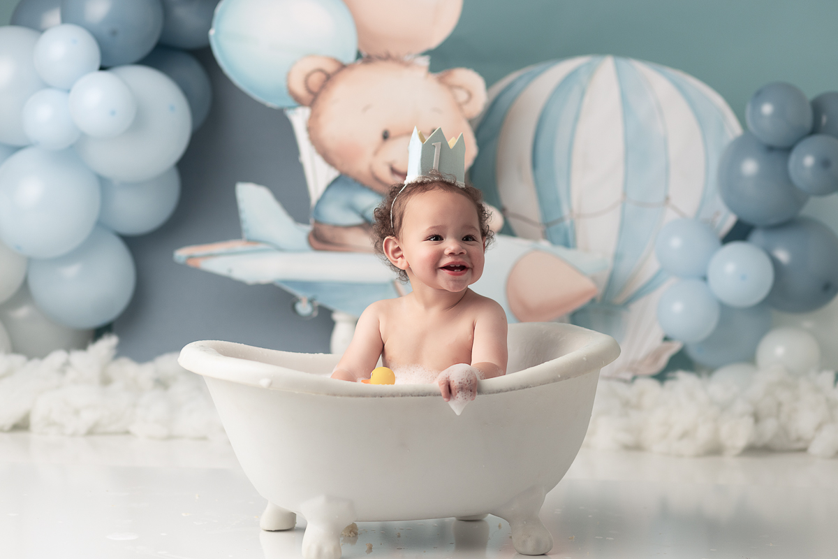 Signature "splash" session photo showing baby boy cleaning up in a stylish tub after his cake smash