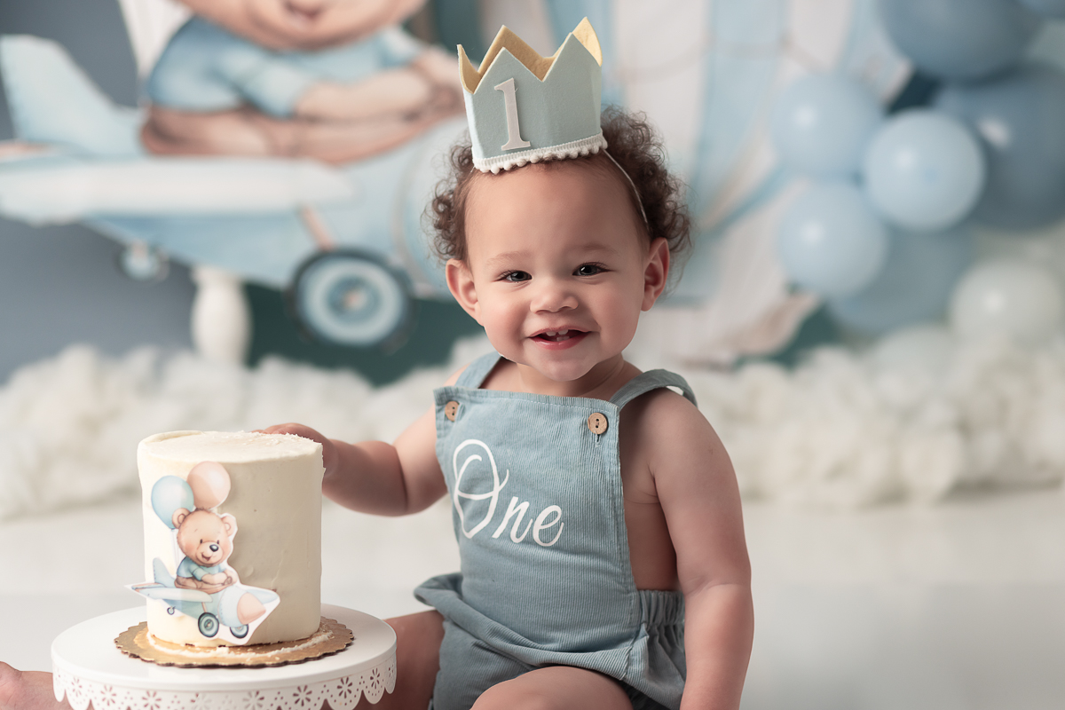 Close-up of baby boy in light blue 'One' romper enjoying his customized cake smash session