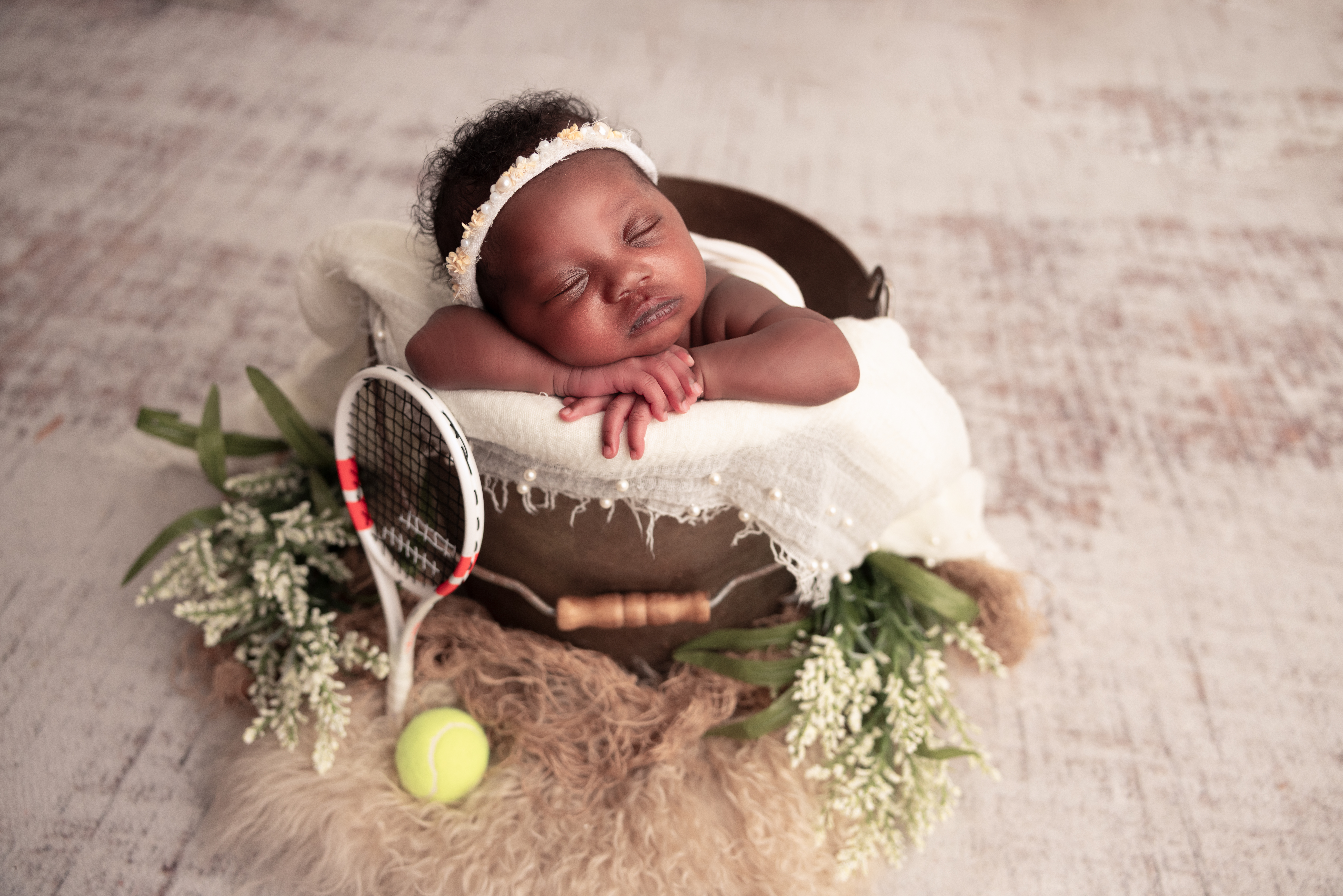 Baby girl in a bucket with a tennis racket and tennis ball