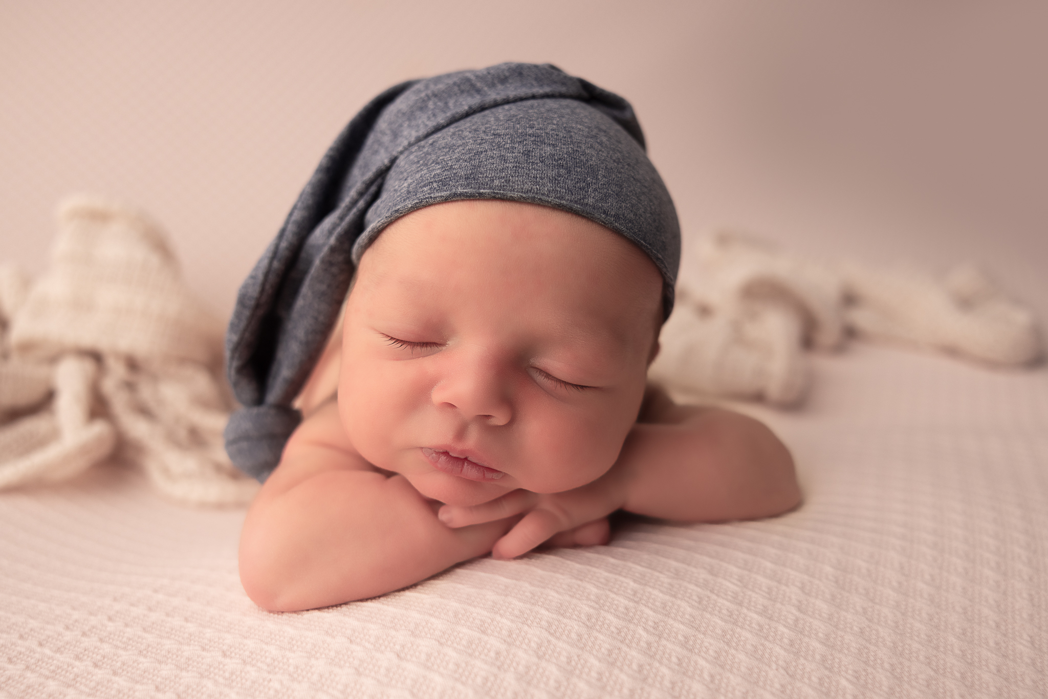 A peaceful newborn with arms crossed with organic draped frabric during a professional photo session in Dublin, Ohio.