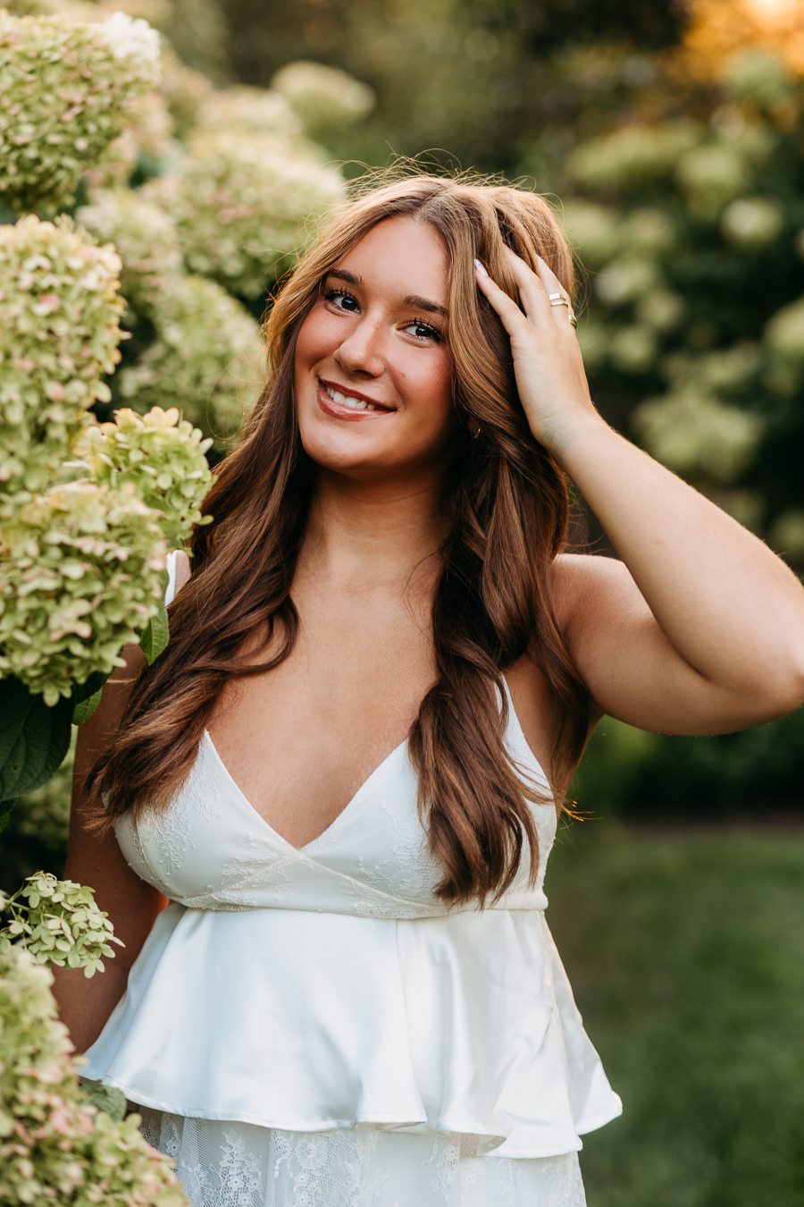 senior high school girl with hand in her hair standing next to beautiful hydrangeas as franklin park conservatory