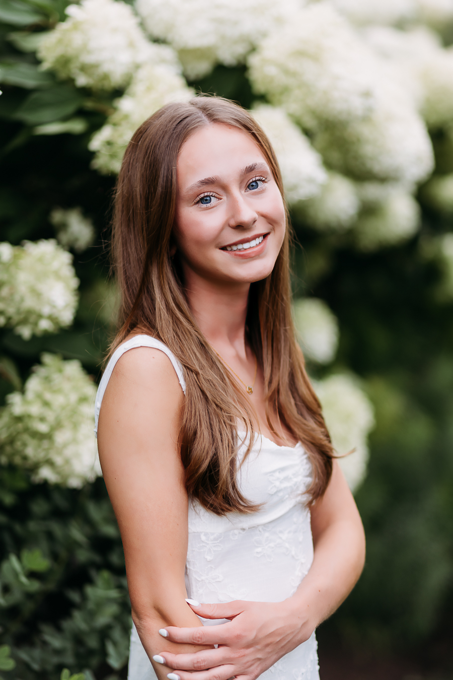 Beautiful high school senior girl standing in front of white hydrangeas at Franklin Park Conservatory for her Senior pictures in a scenic Columbus, Ohio park