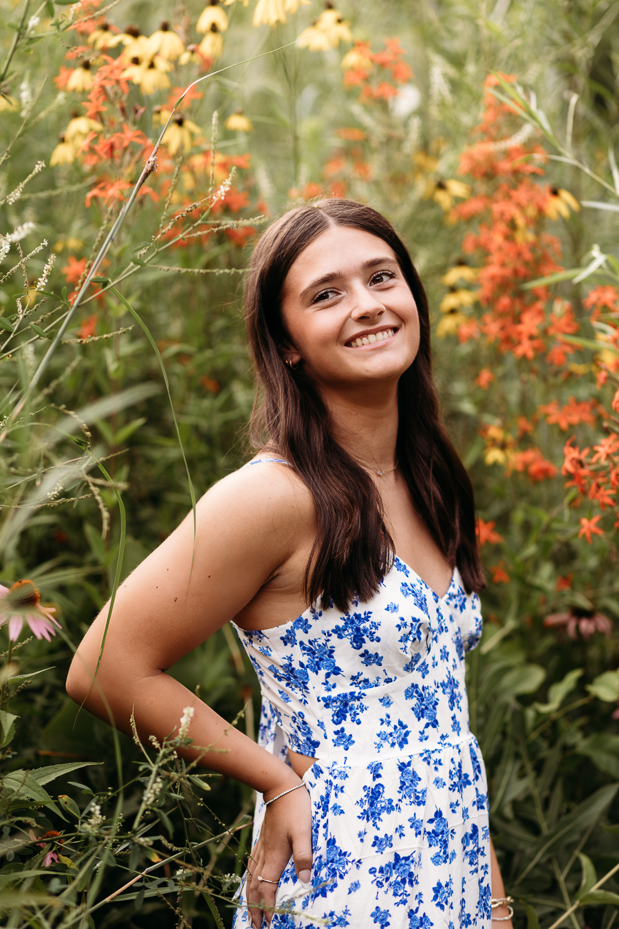 Senior High School Girl in the middle of orange flowers with her hands on her hips wearing a blue and white dress